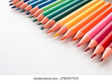 A vibrant array of sharpened wooden pencils in various colors, including blue, green, yellow, orange, pink, and red, are neatly aligned diagonally on a clean white surface, creating a striking visual.