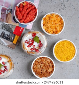 Vibrant assortment of snacks and desserts in white bowls, including spicy chips, cornflakes, vermicelli, and a yogurt parfait topped with pomegranate seeds and mint - Powered by Shutterstock