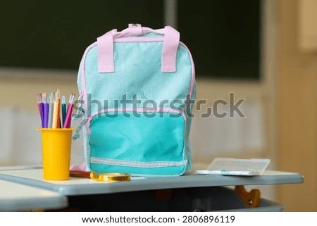 A vibrant backpack sits on a classroom desk, surrounded by bright stationery, signaling the start of lessons and joyful learning in primary school.