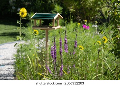 A vibrant blooming garden filled with colorful flowers in full bloom, with a charming wooden birdhouse as the focal point - Powered by Shutterstock