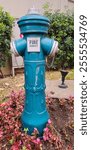 A vibrant blue fire hydrant surrounded by colorful pink flowers, standing in a landscaped urban garden with green bushes and a clean backdrop, ideal for urban and nature photography themes.