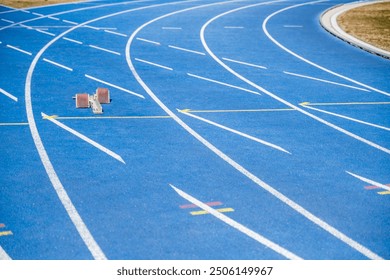 Vibrant blue running track with starting blocks before a race on an empty stadium and textured background - Powered by Shutterstock