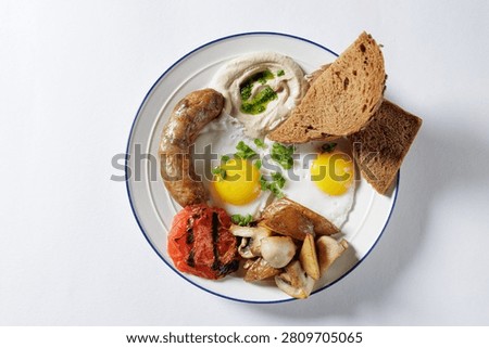 A vibrant breakfast plate featuring fried eggs, sausage, grilled tomatoes, mushrooms, and bread, perfect for food blogs or restaurant menus.