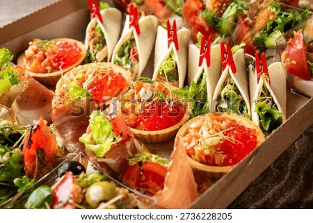 A vibrant catering spread featuring an assortment of mini appetizers, including canapés with red caviar, tiny tacos, and prosciutto wraps, perfect for parties and events