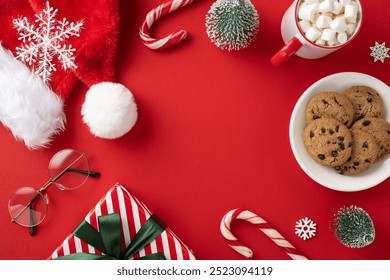 A vibrant Christmas scene with a Santa hat, cookies, marshmallows, and holiday decorations on a red background - Powered by Shutterstock