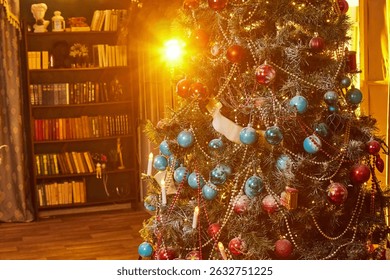 A vibrant Christmas tree adorned with blue and red ornaments sparkles in the warm glow of sunlight. A bookshelf filled with books creates a cozy ambiance in the background.