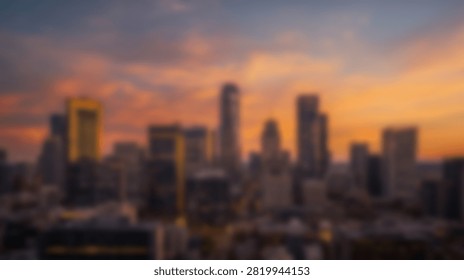 A vibrant cityscape at dusk, featuring a dramatic sunset sky with orange and pink clouds illuminating the silhouettes of tall skyscrapers.