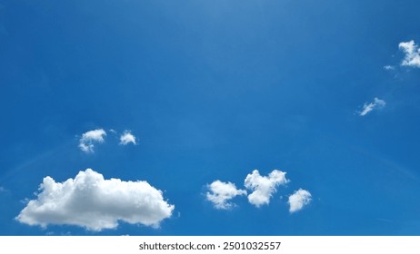 a vibrant, clear blue sky dotted with a few fluffy white cumulus clouds. The sky features a subtle gradient, transitioning from a lighter blue near the top to a deeper blue downward. - Powered by Shutterstock