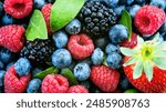 A vibrant close-up of a variety of summer berries, including raspberries, blueberries, blackberries, and a single strawberry. The berries are all different colors and shapes, and they are piled togeth