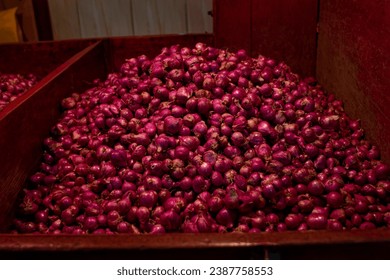 A vibrant, close-up view of a bountiful quantity of fresh red shallots, piled high in a large crate, ready for sale at a bustling market. Ideal for food, cooking, and agricultural themes.