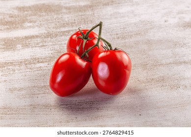 A vibrant cluster of three red cherry tomatoes on a green vine, set against a rustic, light-colored wooden table. Natural lighting highlights their fresh, glossy texture.