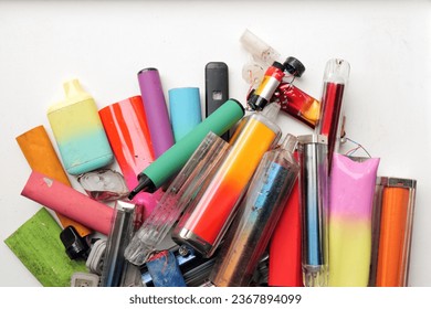 A vibrant collection of discarded electronic cigarette vapes and internal components shot over a white plastic background.