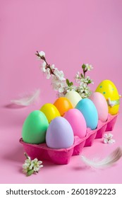 Vibrant collection of painted Easter eggs arranged in a pink basket, adorned with delicate flowers and feathers, set against a soft pink background.