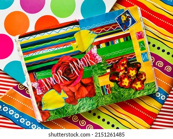 A vibrant colorful scrapbook with a collage (fish, flowers, grass, stripes, geometric ornaments, and cut-out words Amor and May) shot on the background of bright striped wrapping paper.