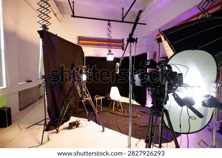 A vibrant creative studio space is prepared for video production, showcasing an organized array of cameras, lights, and a minimalist chair under an eye-catching backdrop.
