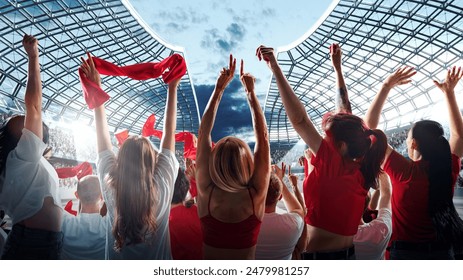 Vibrant crowd of enthusiastic sports fans raises their arms and waves red scarves in celebration against modern stadium with clear sky above. Concept of support, international match, betting, games. - Powered by Shutterstock