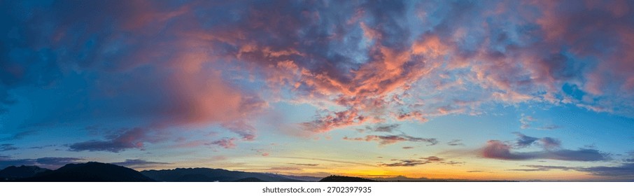Vibrant dawn over mountains with dramatic sunrise cloudscape, soft glow along the horizon.