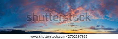 Vibrant dawn over mountains with dramatic sunrise cloudscape, soft glow along the horizon.