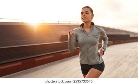 A vibrant and determined young woman joyfully sprints along a scenic track at sunset, perfectly showcasing her unwavering commitment to fitness and overall wellbeing, embodying the essence of health - Powered by Shutterstock