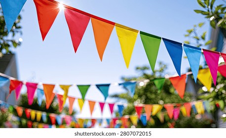 A vibrant display of triangular bunting flags strung across an outdoor area, illuminated by bright sunlight filtering through the leaves of trees.