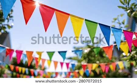 A vibrant display of triangular bunting flags strung across an outdoor area, illuminated by bright sunlight filtering through the leaves of trees.