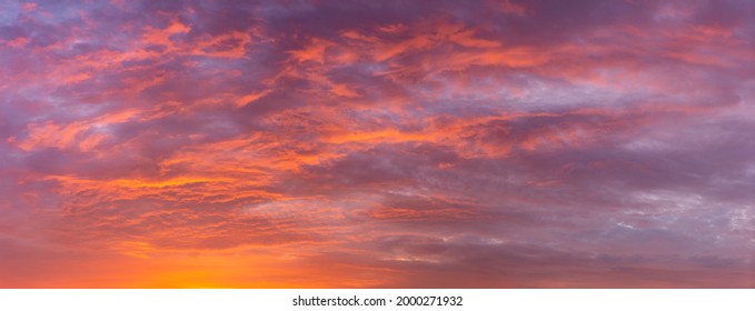 Vibrant dramatic panorama of cloud blanket texture and detail brightly colorful lit up orange from below at sunset with blue tints in the background. Painterly weather condition wallpaper backdrop.