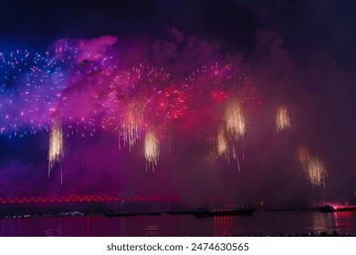  a vibrant fireworks display over a body of water at night in Busan, Korea, with a bridge illuminated in red and colorful reflections. - Powered by Shutterstock