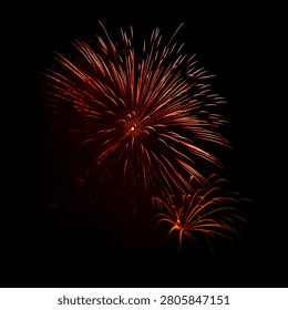 The vibrant fireworks explode over a calm water body, reflecting colorful lights in the night sky.