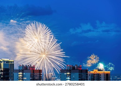 Vibrant fireworks exploding over city apartment buildings at night. Festive celebration display against a blue twilight sky for holiday events