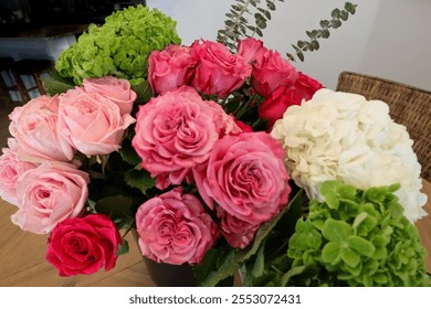 A vibrant floral arrangement featuring pink roses, red roses, white hydrangeas, green hydrangeas, and eucalyptus stems on a wooden table, creating a fresh and elegant display. - Powered by Shutterstock