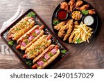 A vibrant food platter featuring gourmet hot dogs with various toppings, a side of crispy chicken tenders, golden french fries, and assorted dipping sauces on a rustic wooden table.