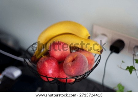 vibrant fruit selection featuring bananas, apples, and peaches in a metal basket against a soft mint green wall with shadow patterns and electrical outlet, serene, abstract, natural, bright