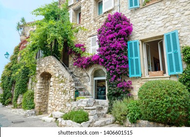 Vibrant Green Ivy And Purple Flowers Grow Over A Medieval Stone Building In France. Ancient Stairs Lead Up To The Entrance Of A Jewelry Store In Saint Paul De Vence. Beautiful Stone Architecture.