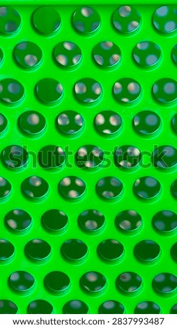 A vibrant green plastic surface with a regular pattern of circular, domed bumps and small holes, creating a textured and reflective industrial background.