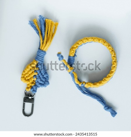 A vibrant, handcrafted macrame keychain and bracelet set, featuring a beautiful interplay of blue and yellow threads, showcased against a pristine white background
