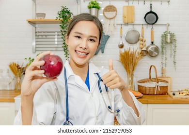 Vibrant and healthy beautiful asian woman nutritionist doctor thumbs up showing red apple, miracle fruit with vitamin C, excellent nutrition, good for health, nutrition advice in the kitchen.