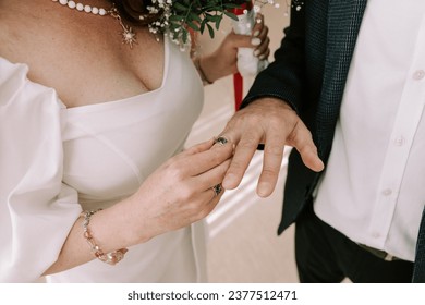 A vibrant horizontal wedding photograph capturing a close-up moment as the bride lovingly slides the ring onto the groom's finger, symbolizing their eternal commitment and love.