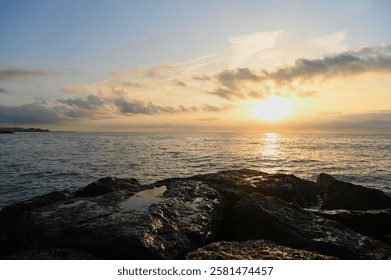 Vibrant hues fill the sky as the sun sets over the tranquil ocean, creating golden reflections on wet rocks along the coastline, inviting serenity and peace. - Powered by Shutterstock - Get 15% off with code: PIKWIZARD15