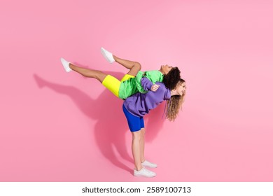 Vibrant image featuring two joyful friends in colorful casual clothing posing playfully against a pink background