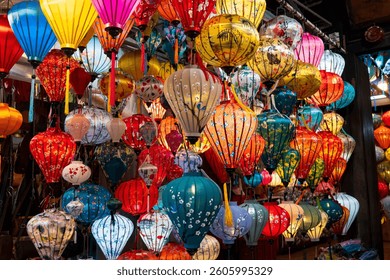 Vibrant, intricately patterned lanterns in assorted shapes and colors hang gracefully along a timeworn Vietnam market, showcasing exquisite traditional artistry.
