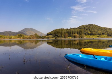 Vibrant kayaks on a serene lake with mountains in the background, reflecting peaceful nature under a clear blue sky. - Powered by Shutterstock