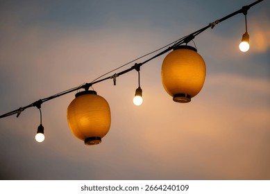 Vibrant lanterns and string lights create a warm, inviting atmosphere during an evening gathering. The soft glow enhances the serene skyline at dusk.
