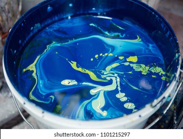 A Vibrant Large Pot Of Blue, Aqua And Greens Mixed Acrylic Block Printing And Screen Printing Paint In A Bucket In An Industrial Creative Art Studio Setting.