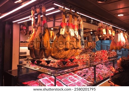 Vibrant market stall displays an array of cured meats, including large Iberian ham legs hanging from the ceiling. 