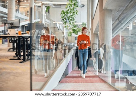 In a vibrant modern startup office, a businesswoman with striking orange hair is immersed in her work at her desk, embodying the dynamic and creative spirit of contemporary entrepreneurship.
