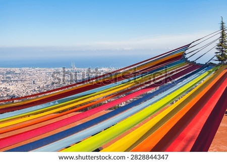 Vibrant multicolored hammocks at an elevated viewpoint overlooking the panoramic cityscape of Barcelona and the Mediterranean Sea. Bright travel image representing relaxation, summer holidays, tourism, and leisure in Catalonia, Spain.
