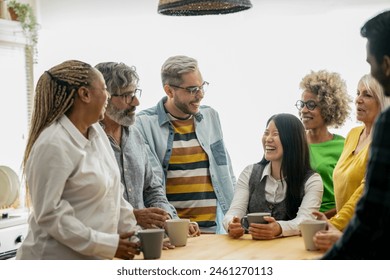 A vibrant, multigenerational team shares laughter and conversation over coffee in a naturally lit, relaxed office setting. - Powered by Shutterstock