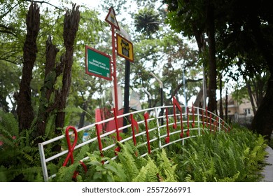 A vibrant musical-themed installation with red notes on a metal fence surrounded by lush green ferns and trees, capturing creativity and urban art in a serene park setting - Powered by Shutterstock