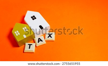 A vibrant orange backdrop features miniature houses atop tiles spelling 
