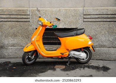 Vibrant orange scooter parked against stone wall on city street - Powered by Shutterstock